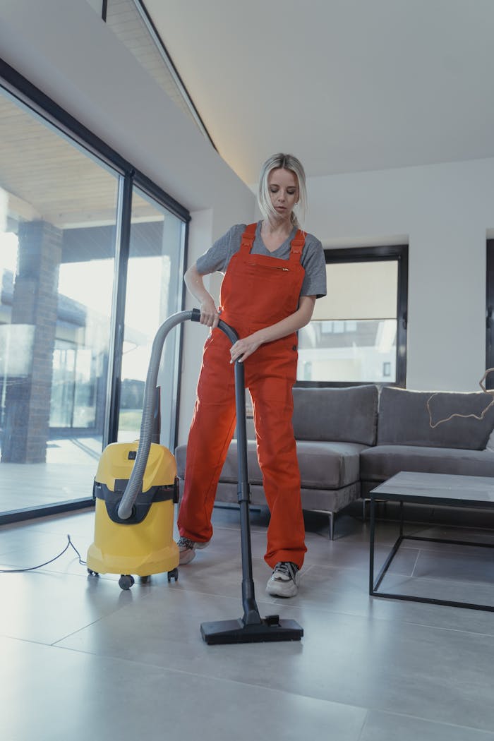 Woman in Orange Jumpsuit and Gray Shirt using Vacuum Cleaner